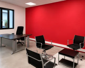 Bureau de direction au BURO Club Partner Beaune avec mur d'accent rouge, bureau en bois foncé et espace d'accueil avec fauteuils noirs.