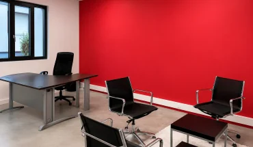Bureau de direction au BURO Club Partner Beaune avec mur d'accent rouge, bureau en bois foncé et espace d'accueil avec fauteuils noirs.