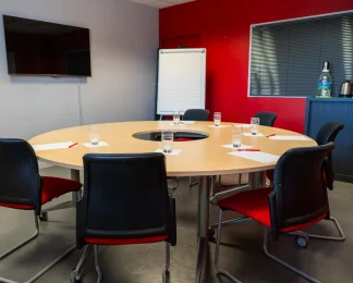 Salle de réunion avec table ronde, écran TV et mur rouge au BURO Club Le Mans