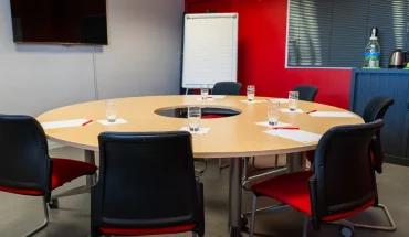 Salle de réunion avec table ronde, écran TV et mur rouge au BURO Club Le Mans