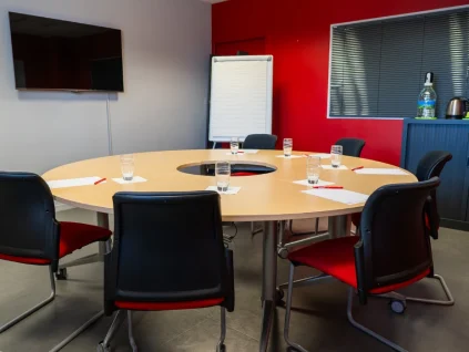 Salle de réunion avec table ronde, écran TV et mur rouge au BURO Club Le Mans
