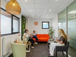 Salon d'accueil du centre BURO Club Vannes Laroiseau, avec canapé orange, fauteuils, mur végétal et suspension en osier ; trois personnes patientent en lisant.