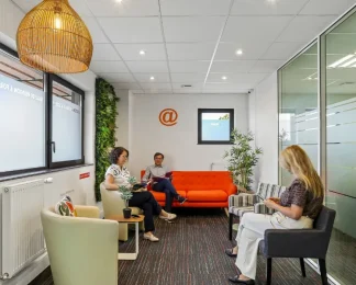 Salon d'accueil du centre BURO Club Vannes Laroiseau, avec canapé orange, fauteuils, mur végétal et suspension en osier ; trois personnes patientent en lisant.