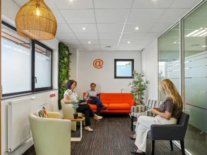 Salon d'accueil du centre BURO Club Vannes Laroiseau, avec canapé orange, fauteuils, mur végétal et suspension en osier ; trois personnes patientent en lisant.