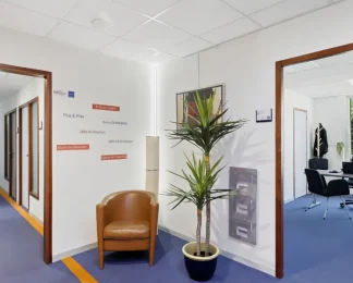 Hall du centre BURO Club Vannes Ténénio avec signalétique des services (bureaux équipés, salles de réunion et de formation, coworking), fauteuil camel et plante, ouvert sur un bureau.