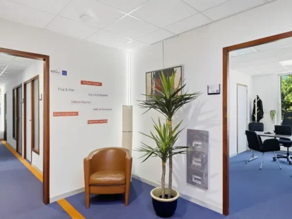 Hall du centre BURO Club Vannes Ténénio avec signalétique des services (bureaux équipés, salles de réunion et de formation, coworking), fauteuil camel et plante, ouvert sur un bureau.