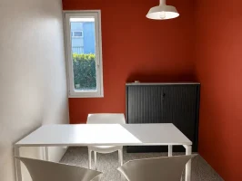 Petit espace de travail ou salle d'entretien avec des murs rouge brique, une table blanche, deux chaises et une armoire de rangement métallique noire.