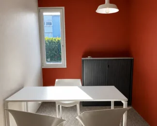 Petit espace de travail ou salle d'entretien avec des murs rouge brique, une table blanche, deux chaises et une armoire de rangement métallique noire.