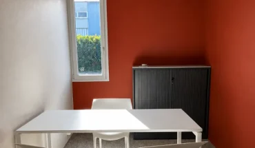 Petit espace de travail ou salle d'entretien avec des murs rouge brique, une table blanche, deux chaises et une armoire de rangement métallique noire.
