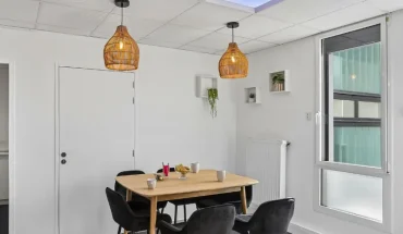 Coin repas du centre BURO Club Vannes Ténénio, avec table en bois, chaises noires, suspensions en osier, étagères avec plantes et plafond imitant un ciel.