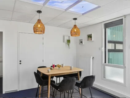 Coin repas du centre BURO Club Vannes Ténénio, avec table en bois, chaises noires, suspensions en osier, étagères avec plantes et plafond imitant un ciel.